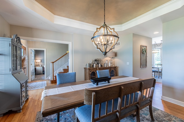 dining space featuring light wood-type flooring, a tray ceiling, an inviting chandelier, and crown molding