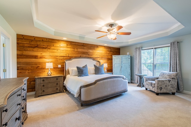 carpeted bedroom with a tray ceiling, ceiling fan, wood walls, and ornamental molding