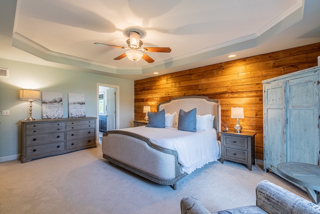 carpeted bedroom with wood walls, a raised ceiling, crown molding, ceiling fan, and connected bathroom