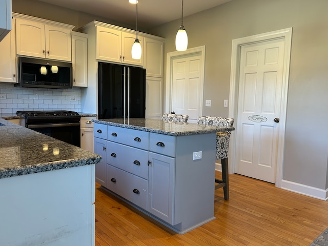 kitchen with black appliances, light wood-type flooring, white cabinetry, and hanging light fixtures