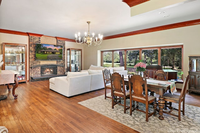 dining space featuring a notable chandelier, a fireplace, crown molding, hardwood / wood-style floors, and brick wall