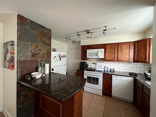 kitchen with decorative backsplash, dark stone countertops, rail lighting, light tile patterned floors, and white appliances