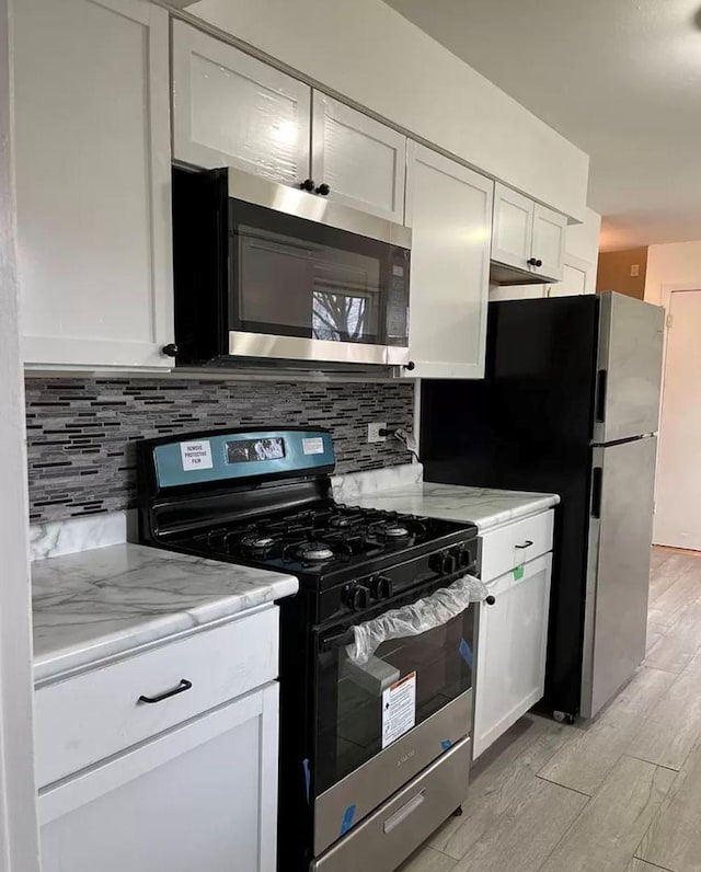 kitchen with appliances with stainless steel finishes, white cabinets, light stone counters, and decorative backsplash