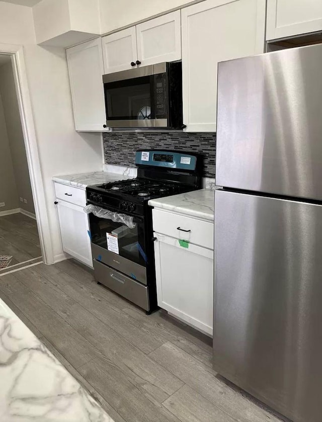 kitchen featuring light stone counters, tasteful backsplash, light wood-type flooring, appliances with stainless steel finishes, and white cabinets