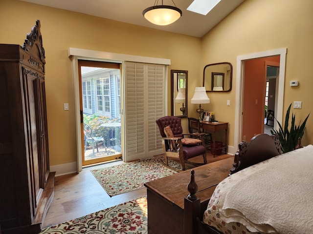 bedroom with light hardwood / wood-style floors, access to outside, and lofted ceiling with skylight