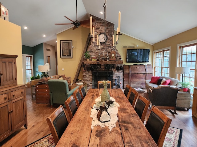 dining area featuring light wood-type flooring, lofted ceiling, a brick fireplace, and ceiling fan