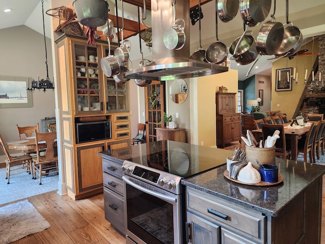 kitchen featuring hanging light fixtures, dark stone countertops, vaulted ceiling, stainless steel range with electric cooktop, and light hardwood / wood-style floors