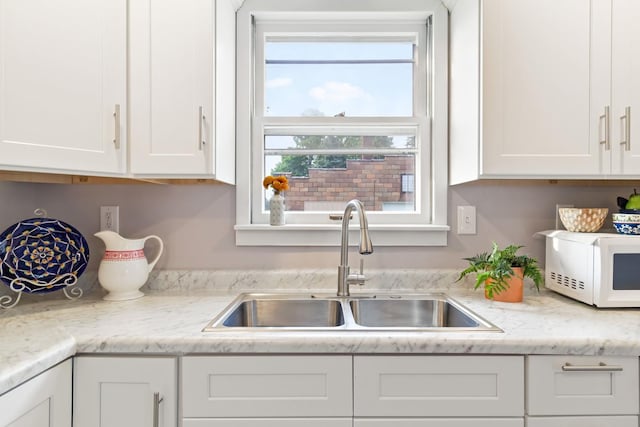 kitchen featuring sink, light stone countertops, and white cabinets