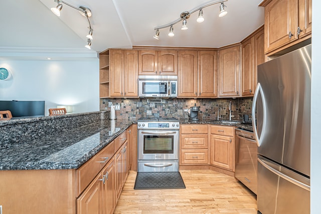 kitchen with appliances with stainless steel finishes, sink, backsplash, dark stone countertops, and light hardwood / wood-style floors