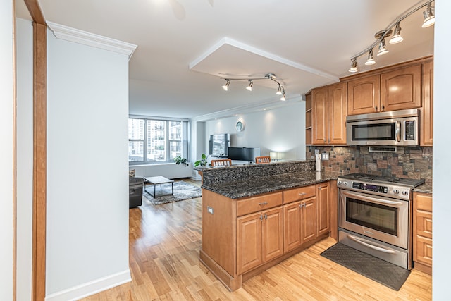 kitchen with kitchen peninsula, dark stone countertops, backsplash, ornamental molding, and stainless steel appliances