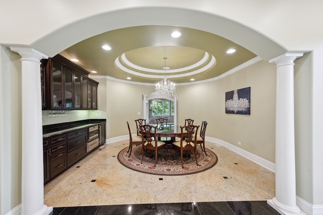 dining space featuring a raised ceiling, ornate columns, ornamental molding, and an inviting chandelier