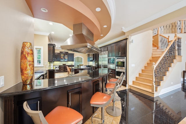 kitchen featuring dark tile patterned flooring, dark brown cabinets, backsplash, ornamental molding, and island range hood