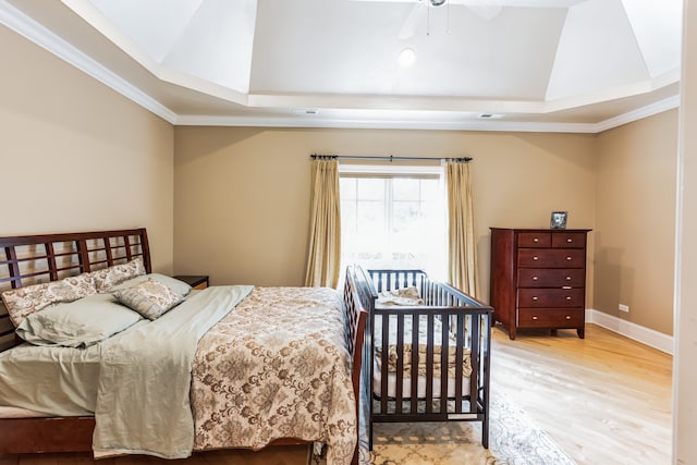 bedroom featuring light hardwood / wood-style flooring, ornamental molding, ceiling fan, and a raised ceiling