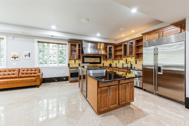 kitchen with tasteful backsplash, appliances with stainless steel finishes, sink, wall chimney range hood, and a kitchen island