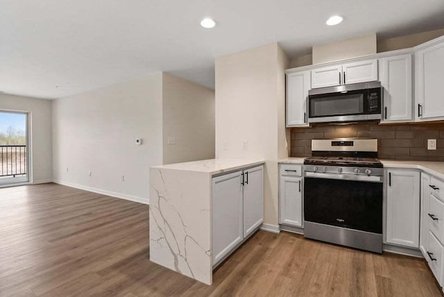 kitchen with tasteful backsplash, white cabinets, light wood-style flooring, a peninsula, and stainless steel appliances