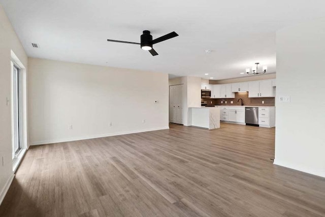 unfurnished living room featuring ceiling fan with notable chandelier, baseboards, and wood finished floors