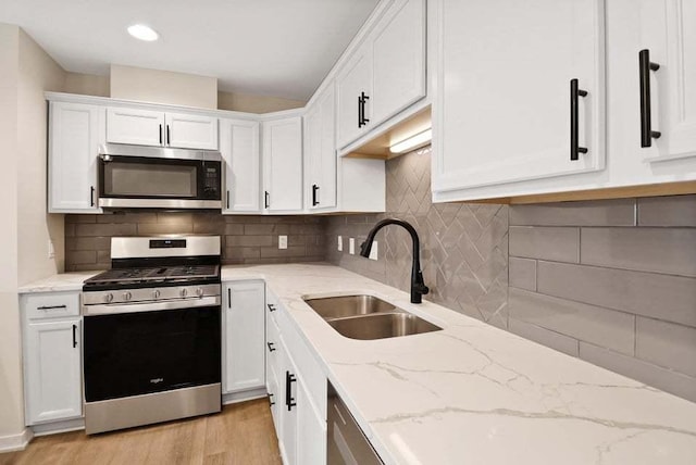 kitchen with white cabinets, light stone countertops, stainless steel appliances, and a sink