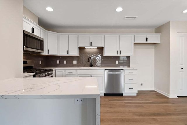 kitchen featuring stainless steel appliances, a sink, white cabinetry, and light stone countertops