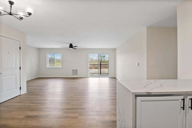 unfurnished living room featuring light wood-type flooring, plenty of natural light, visible vents, and ceiling fan with notable chandelier