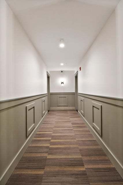 hallway featuring a wainscoted wall and dark colored carpet