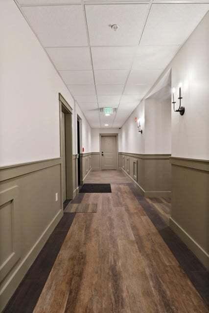 corridor with dark wood-type flooring, a paneled ceiling, and wainscoting