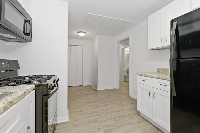 kitchen with range with gas stovetop, black refrigerator, white cabinets, light wood-type flooring, and light stone countertops