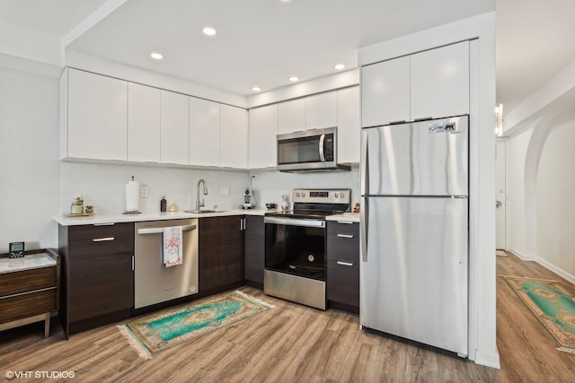 kitchen featuring white cabinetry, dark brown cabinets, tasteful backsplash, light wood-type flooring, and appliances with stainless steel finishes