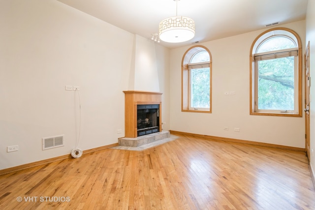 unfurnished living room with a tiled fireplace, a wealth of natural light, and light wood-type flooring