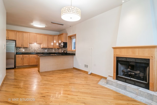 kitchen featuring light wood-type flooring, kitchen peninsula, stainless steel appliances, pendant lighting, and a tile fireplace