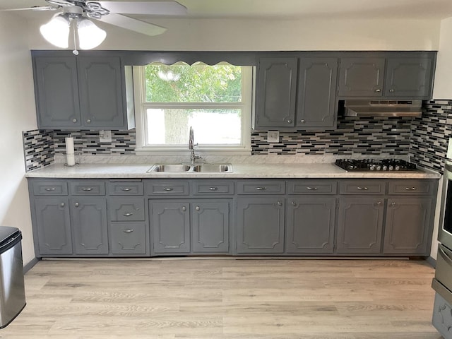 kitchen with sink, gray cabinetry, stainless steel gas stovetop, light hardwood / wood-style floors, and decorative backsplash