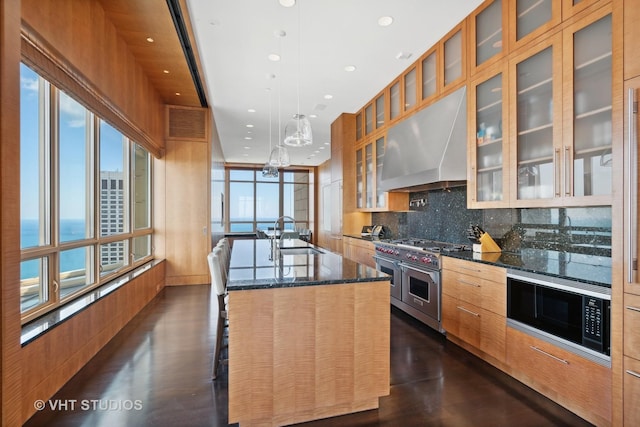 kitchen with range with two ovens, an island with sink, range hood, built in microwave, and a sink