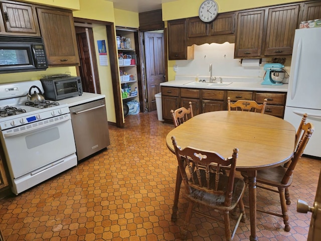 kitchen featuring tile patterned floors, dark brown cabinetry, white appliances, and sink