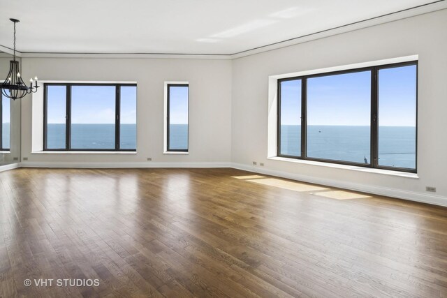 empty room with a water view, a wealth of natural light, hardwood / wood-style floors, and a chandelier