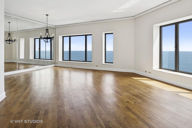 empty room featuring dark hardwood / wood-style flooring, a water view, and an inviting chandelier