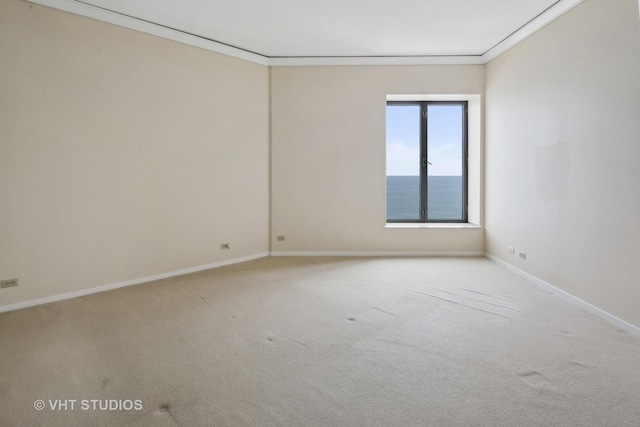 empty room with crown molding, a water view, and light carpet