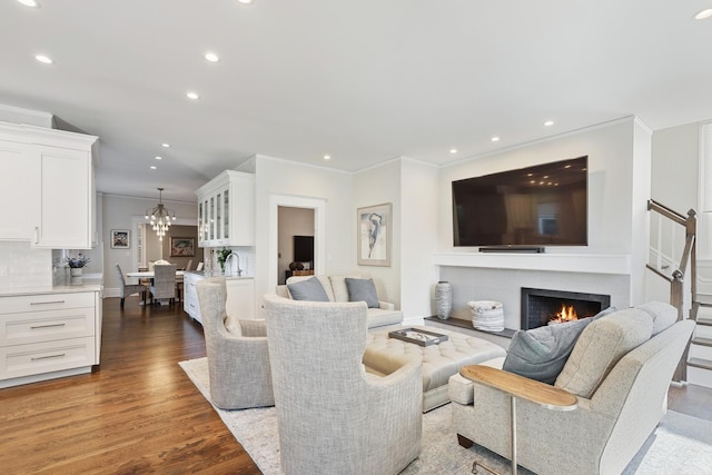 living room featuring a warm lit fireplace, ornamental molding, wood finished floors, and recessed lighting