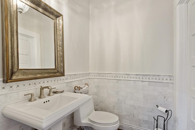 half bathroom with toilet, tile walls, a sink, and wainscoting