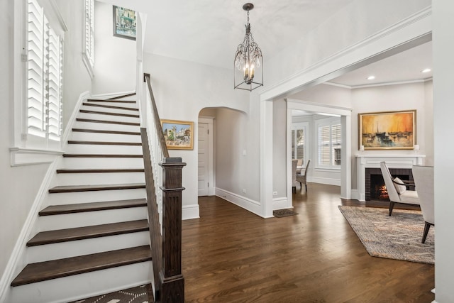 entryway featuring arched walkways, baseboards, stairway, wood finished floors, and a lit fireplace