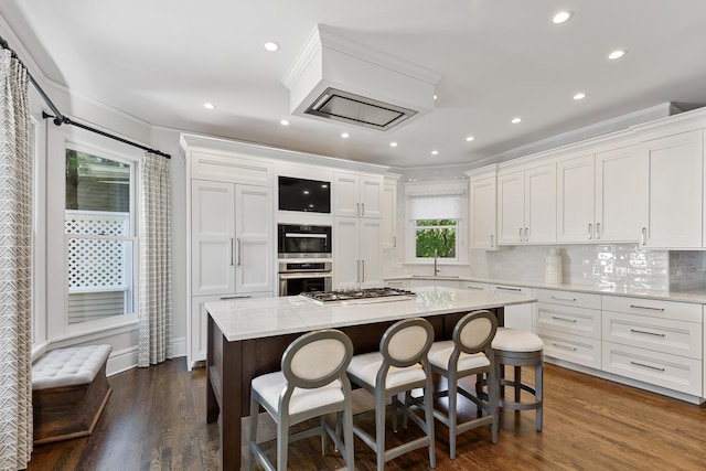 kitchen featuring stainless steel appliances, white cabinetry, a sink, a kitchen island, and a kitchen bar