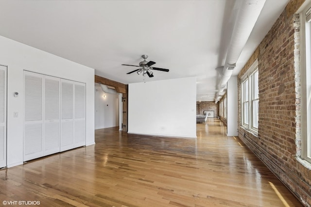 unfurnished living room featuring ceiling fan, wood-type flooring, a brick fireplace, and brick wall