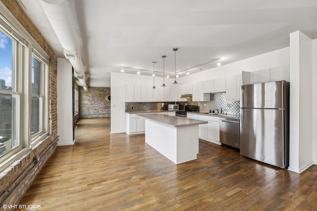 kitchen with brick wall, a kitchen island, white cabinetry, stainless steel appliances, and hanging light fixtures