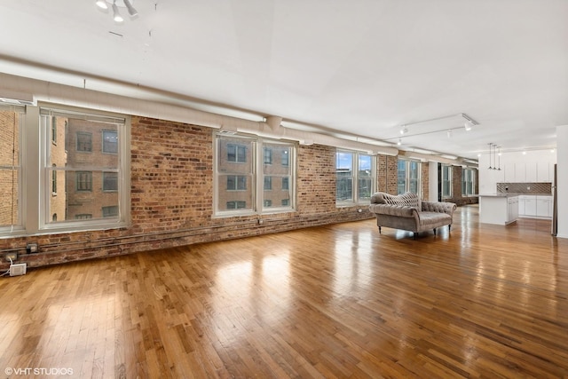 unfurnished living room with light wood-type flooring and brick wall