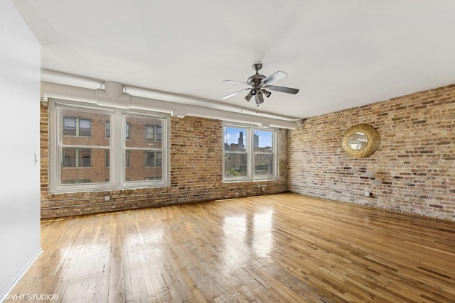 unfurnished room with ceiling fan, brick wall, and light wood-type flooring