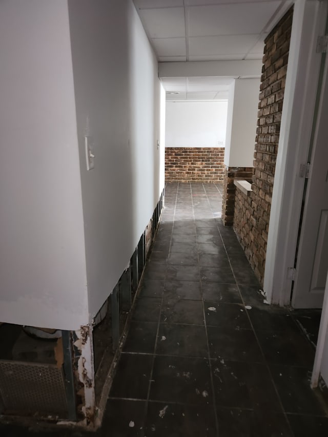 hallway featuring a paneled ceiling and brick wall