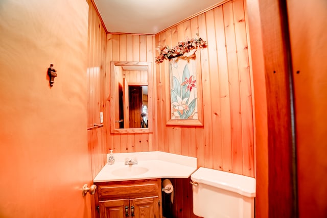 bathroom with wood walls, toilet, and vanity