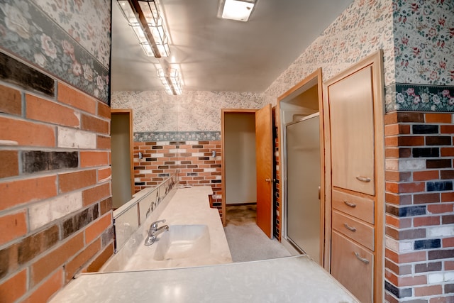 bathroom featuring walk in shower, brick wall, and sink