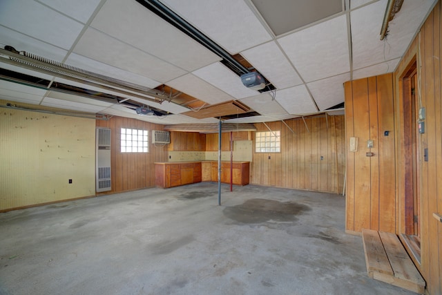 basement with wood walls, a wall unit AC, and a paneled ceiling