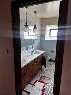 bathroom featuring decorative backsplash, tile walls, toilet, tile patterned flooring, and dual vanity