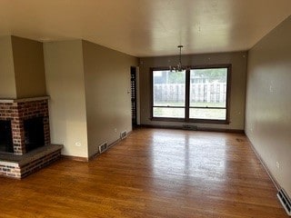 unfurnished living room featuring a fireplace, hardwood / wood-style flooring, and an inviting chandelier