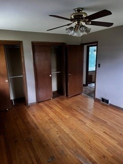 unfurnished bedroom featuring light wood-type flooring, two closets, and ceiling fan